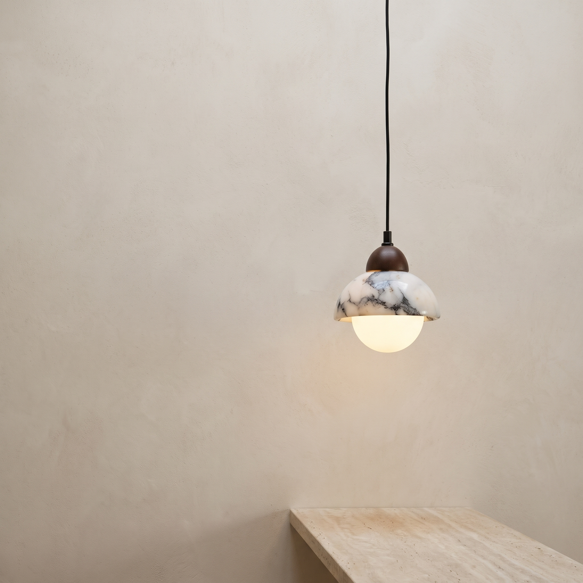 Marble and opal glass pendant lamp with a walnut cap, hanging above a travertine counter